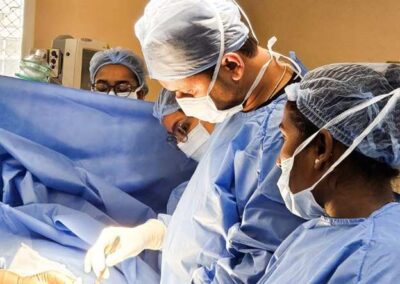 A surgical team in blue scrubs and masks performing an operation under bright overhead lights in an operating room.